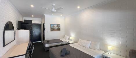 A hotel room with two beds, a desk, a chair, a TV, and a ceiling fan.