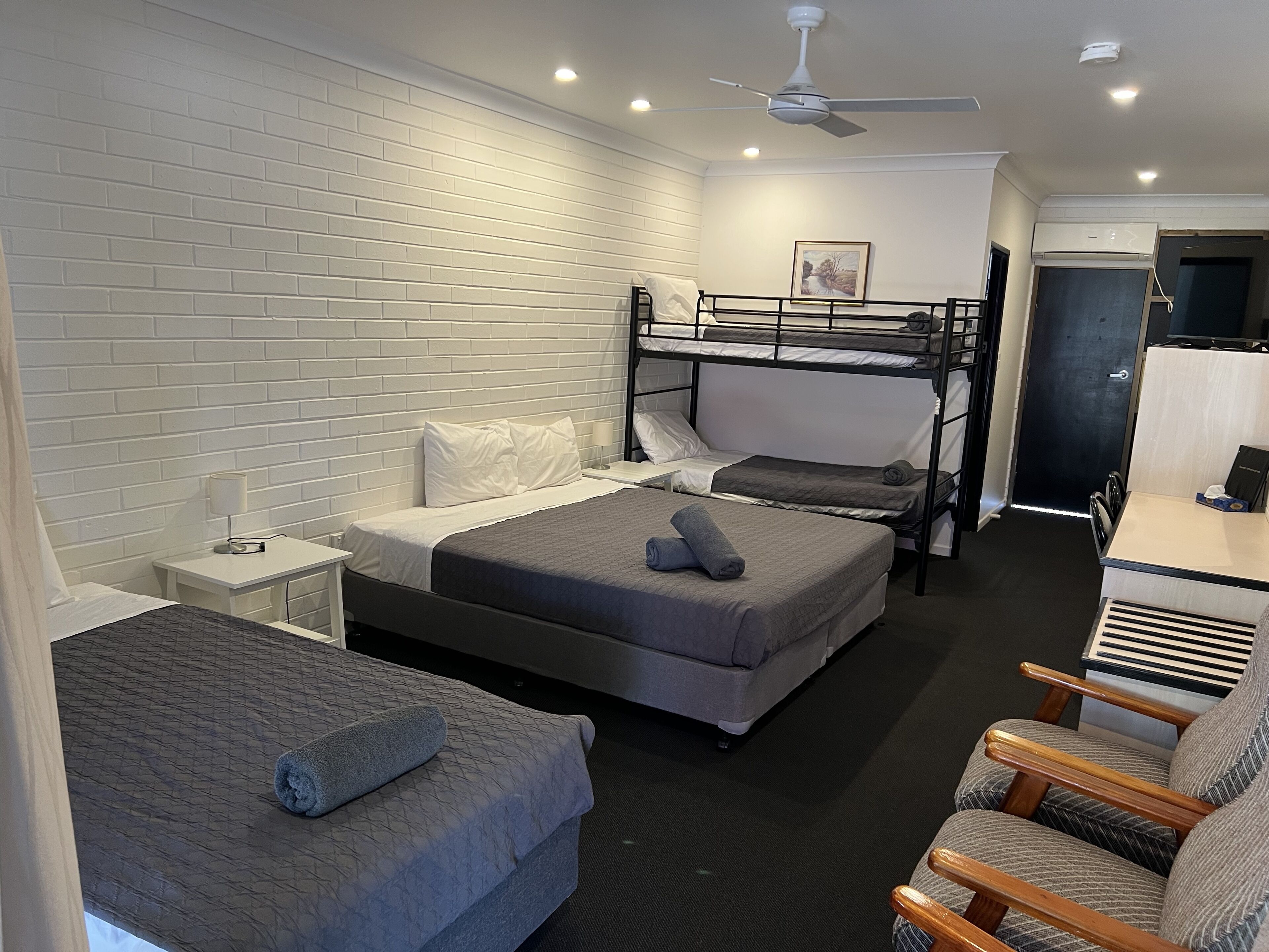 Una habitación de hotel con una cama nido, una cama individual, un escritorio con silla y un ventilador de techo.