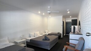 Une chambre d’hôtel avec deux lits, un coin salon avec des fauteuils, un ventilateur de plafond et un téléviseur à écran plat.