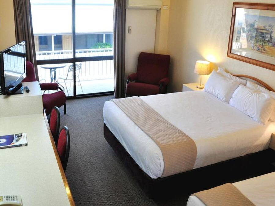 A hotel room with a bed, a desk, a chair, a TV, and a balcony with a table and chairs.