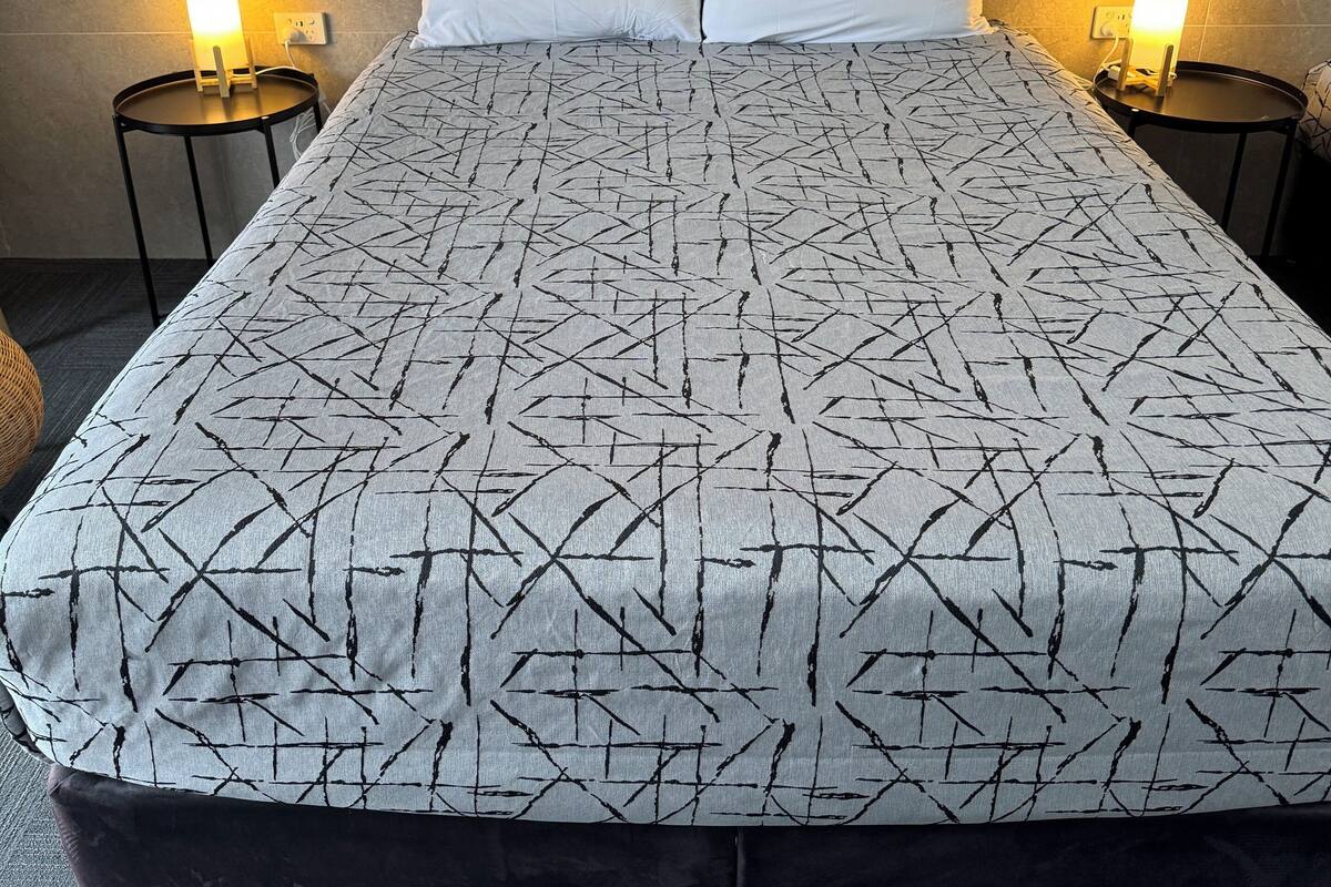 Una cama doble con una colcha de estampado geométrico, dos almohadas blancas y dos lámparas de noche sobre mesitas redondas.