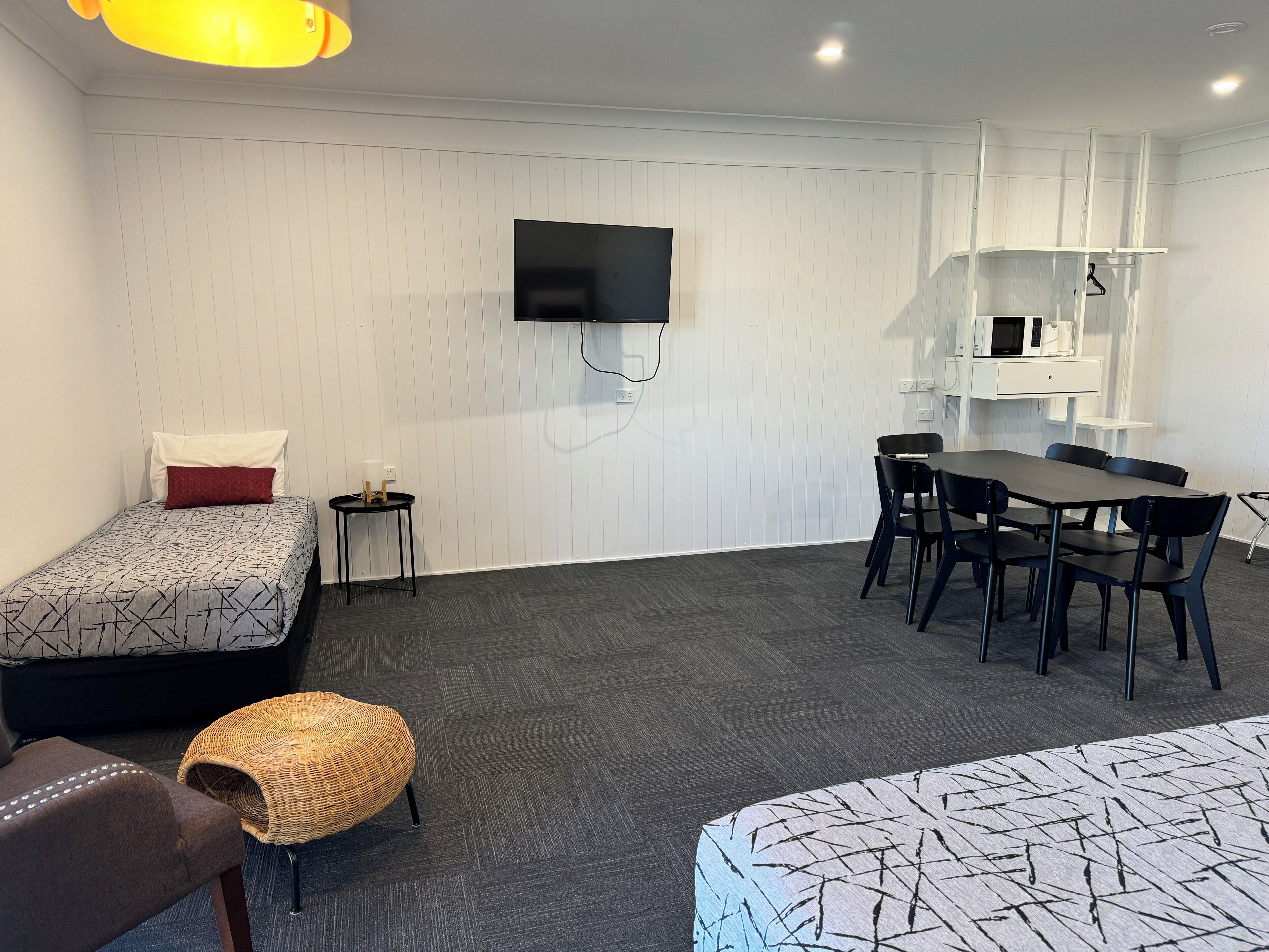 A modern hotel room with a bed, a small table with chairs, a TV mounted on the wall, and a microwave in a cabinet.