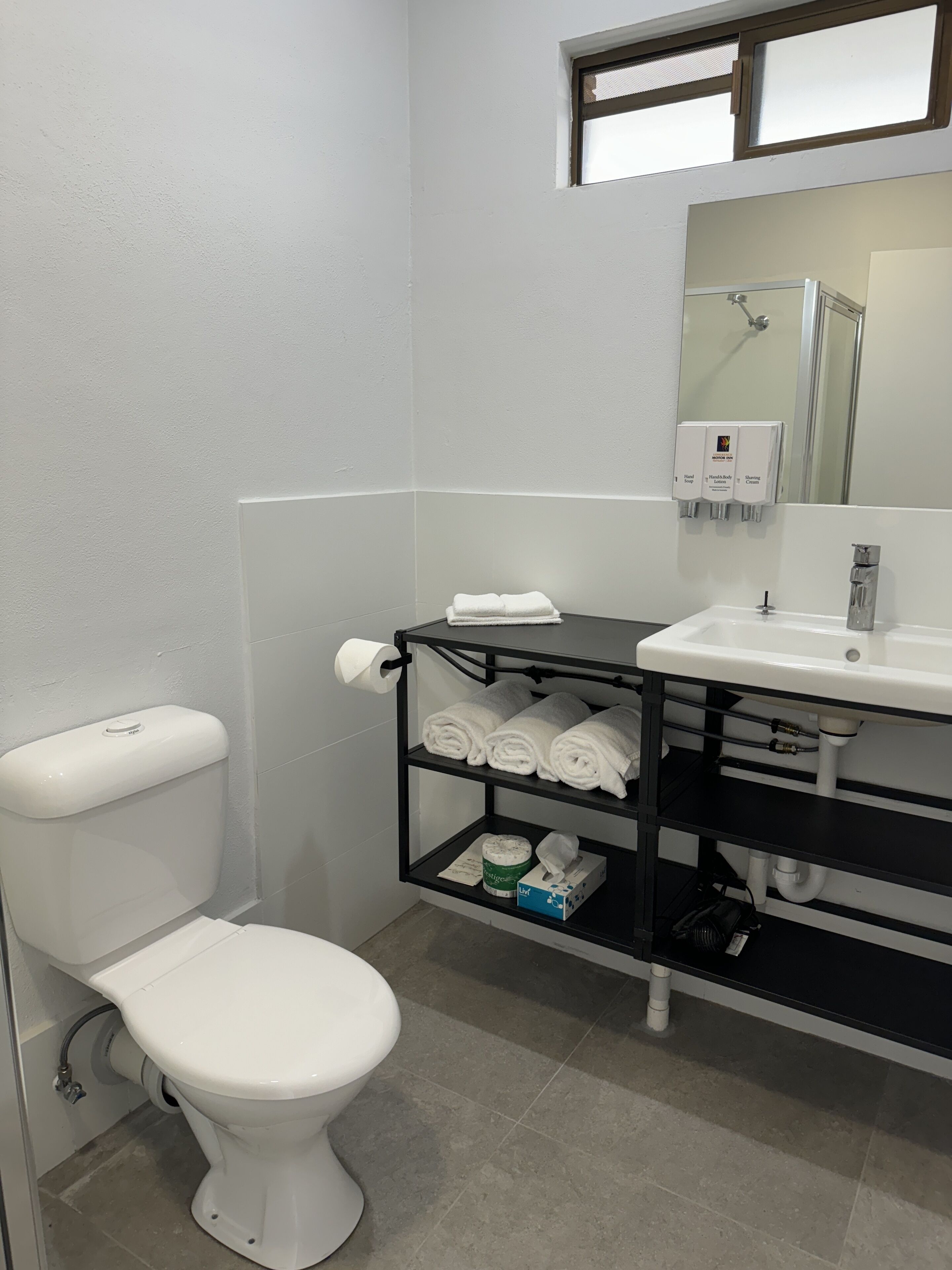 A bathroom with a toilet, a sink, and a shelf with towels and toiletries.