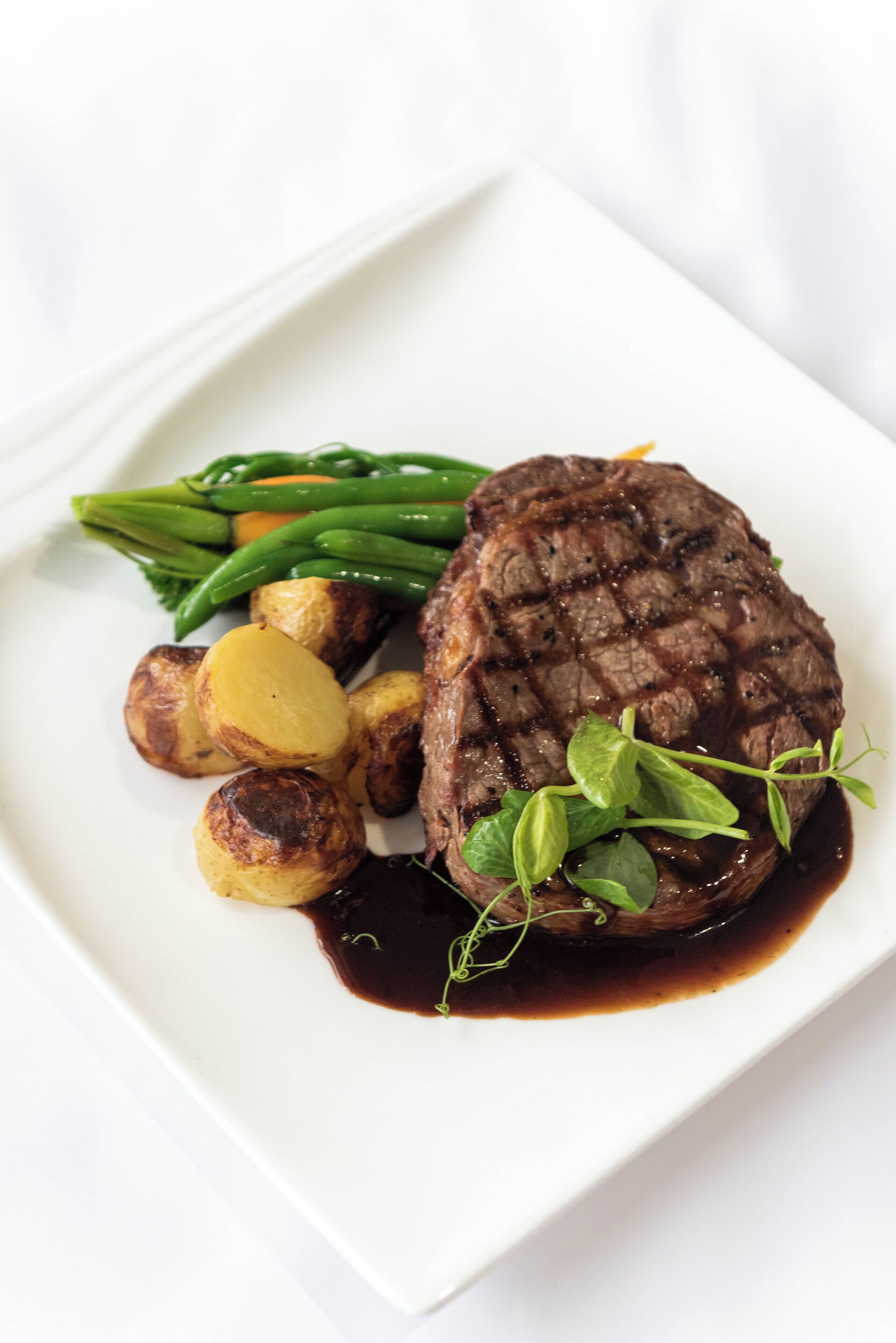 A plate with a grilled steak, roasted potatoes, green beans, and a garnish of herbs.