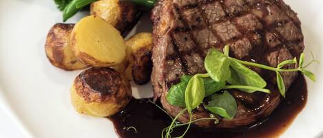 A plate with a grilled steak, roasted potatoes, green beans, and a garnish of herbs.