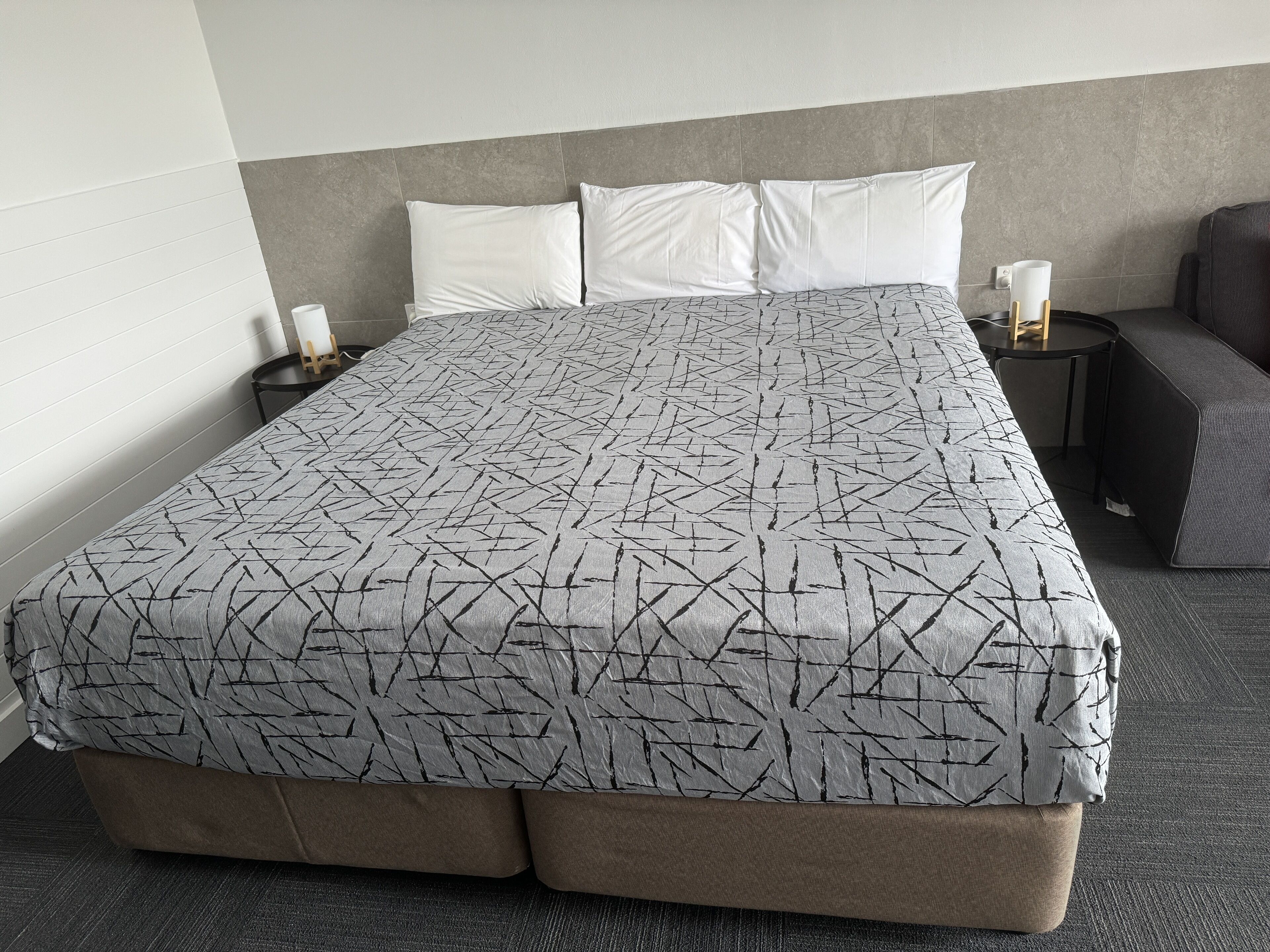 A hotel room with a large bed, a bedside table with a lamp, and a small seating area.