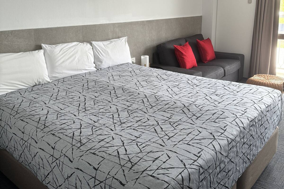 Una habitación de hotel con una cama grande, un sofá gris y una mesita.