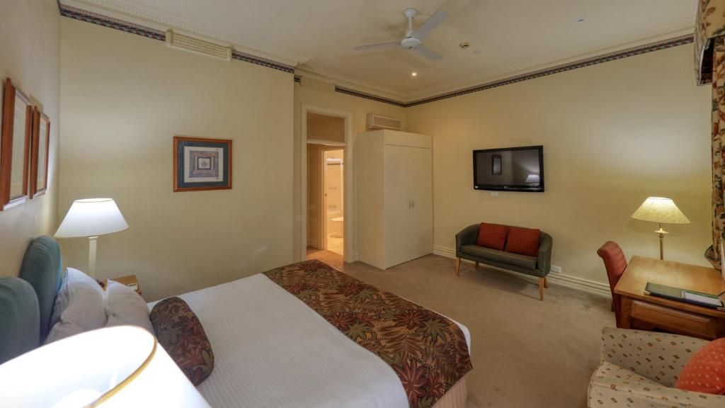 A hotel room with a bed, a desk, a chair, a television, and a wardrobe.
