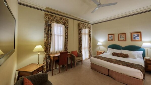 A hotel room with a bed, a desk, a chair, a nightstand, and a ceiling fan. - Royal Exchange Hotel (Broken Hill)