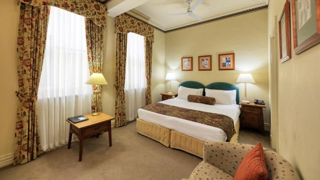 A hotel room with a bed, two bedside tables, a chair, and curtains.