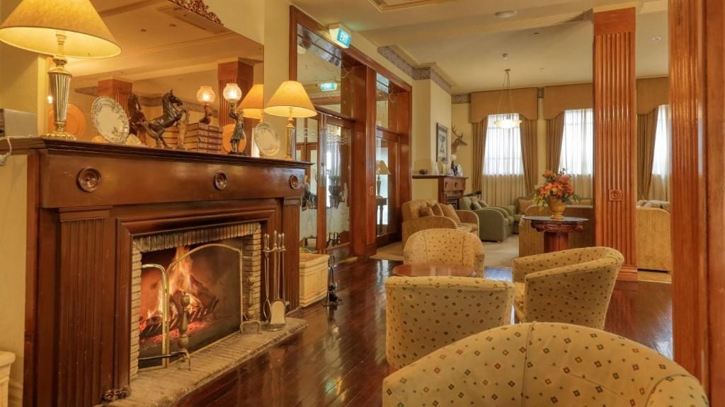 A traditional hotel lobby with a fireplace, comfortable seating, and a mirror reflecting the room.