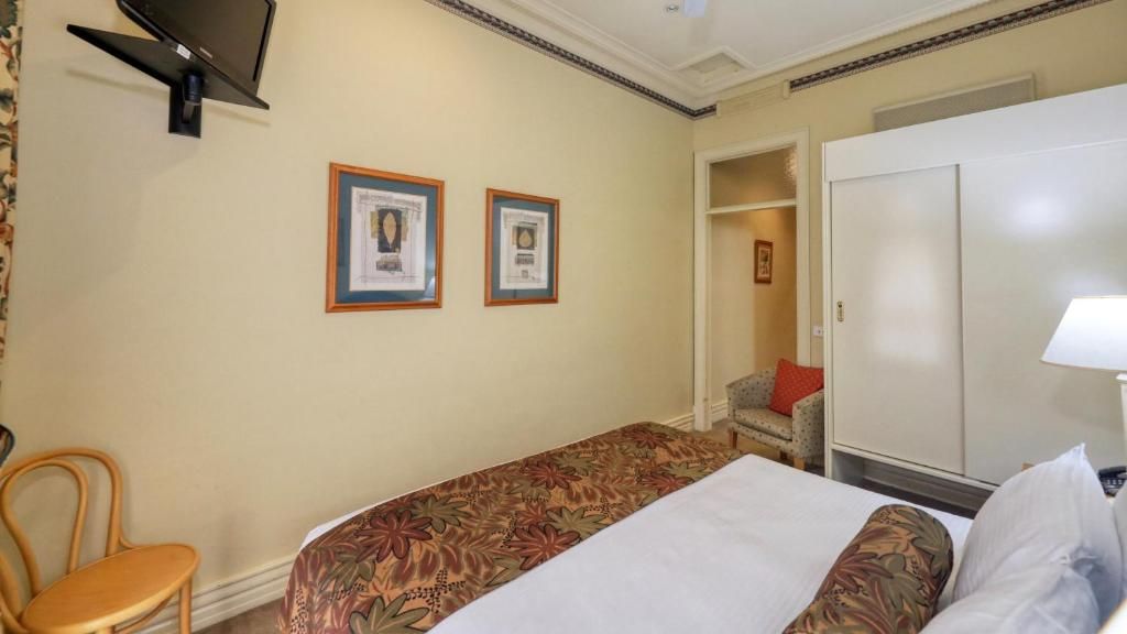 Une chambre d’hôtel équipée d’un lit, d’une chaise, d’une armoire et d’un téléviseur fixé au mur.