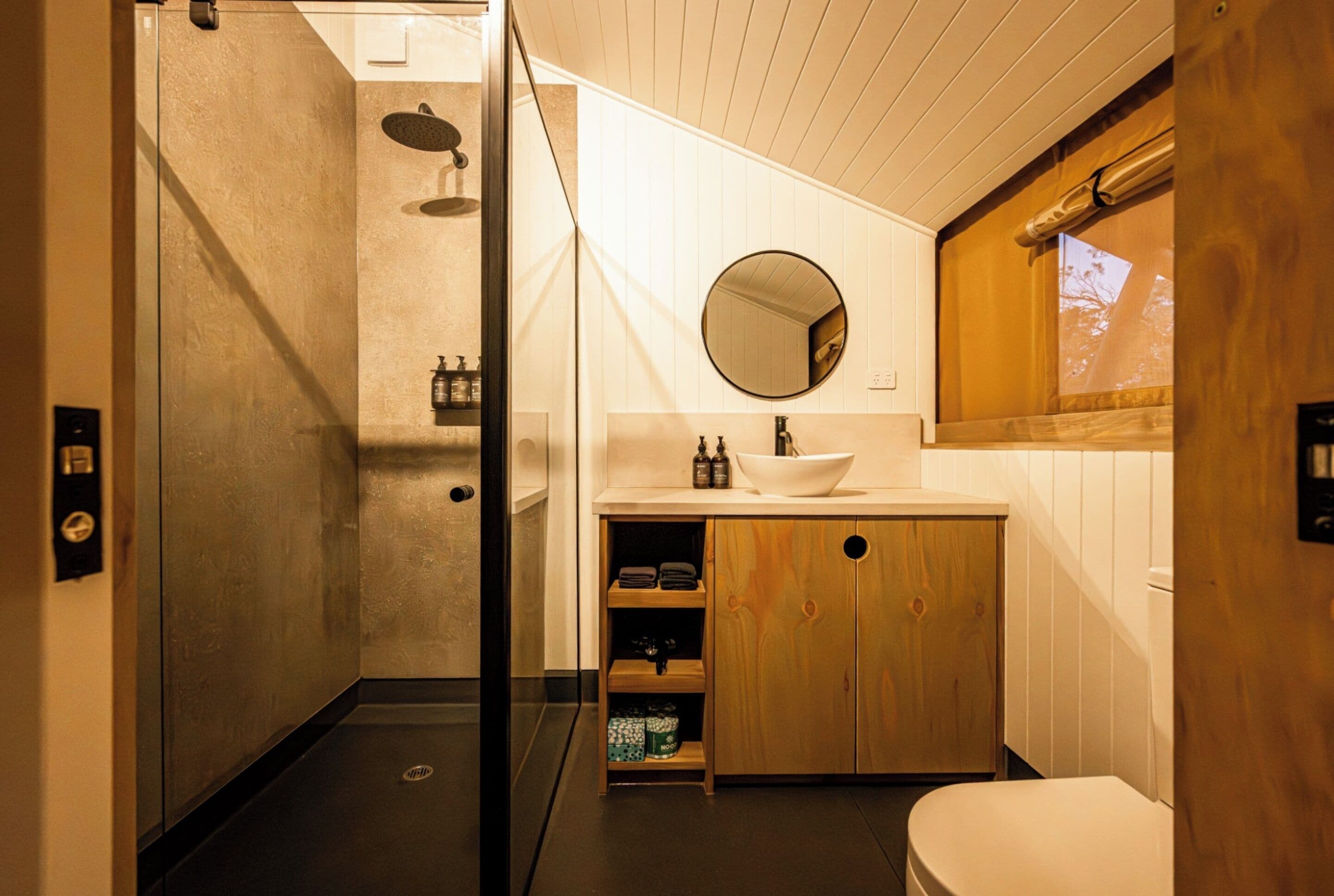 A bathroom with a shower, sink, mirror, and wooden cabinets.