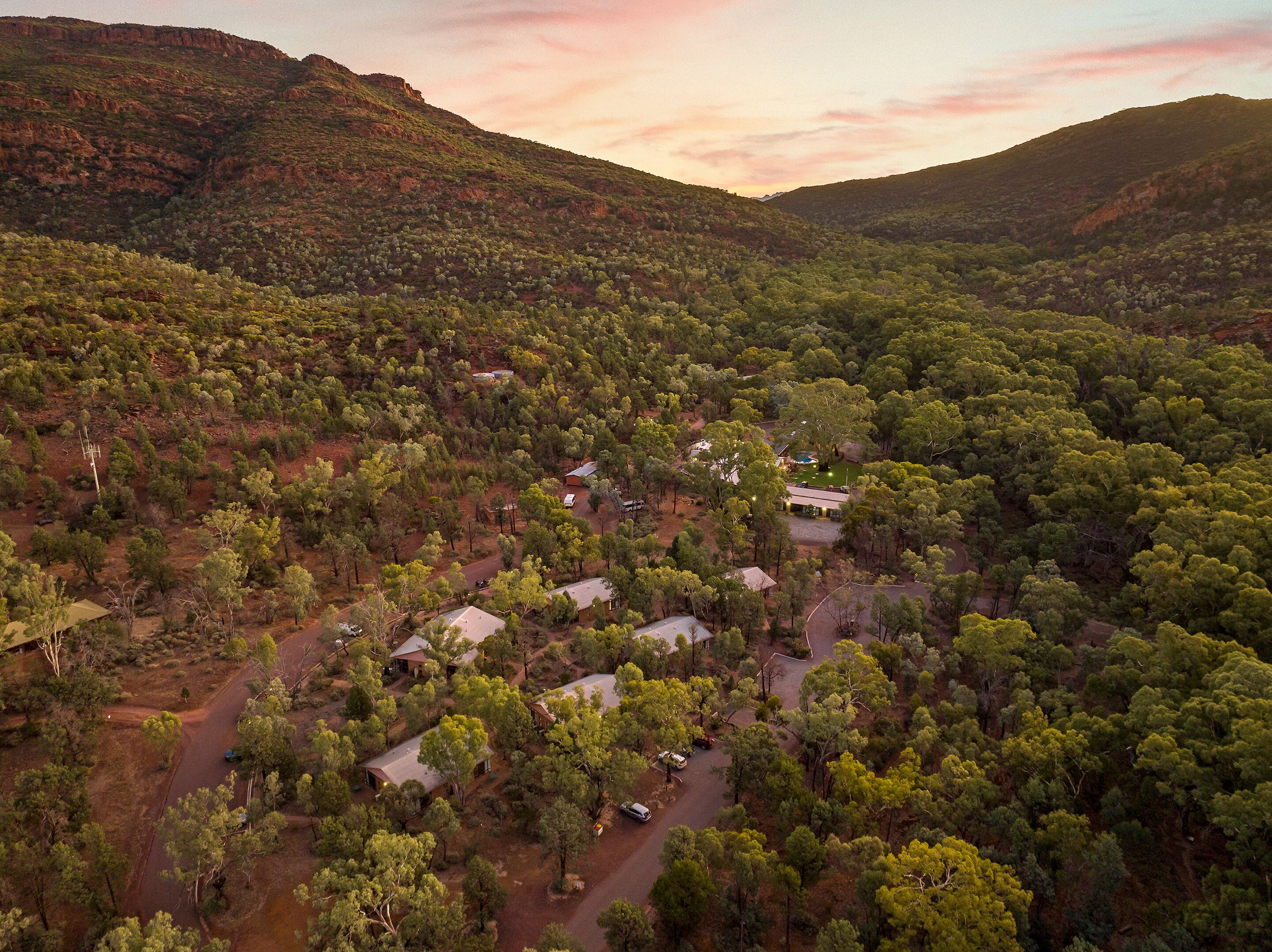 An aerial view of a rural area with scattered houses surrounded by dense vegetation and hills in the background.