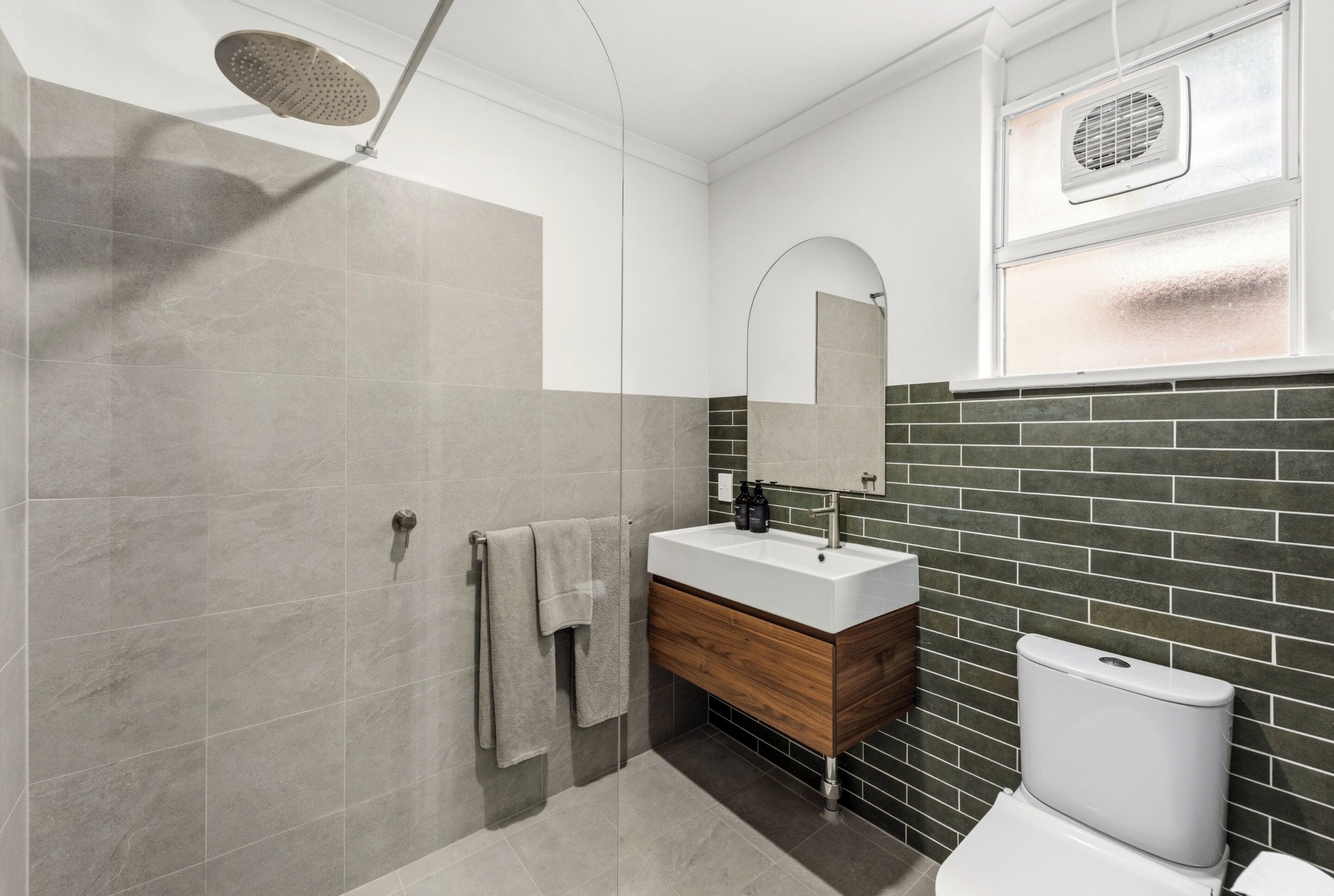 Een moderne badkamer met een douche, wastafel, spiegel en toilet.