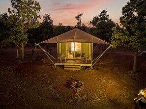 A tented accommodation with a wooden deck, a fire pit, and a view of the surrounding trees.