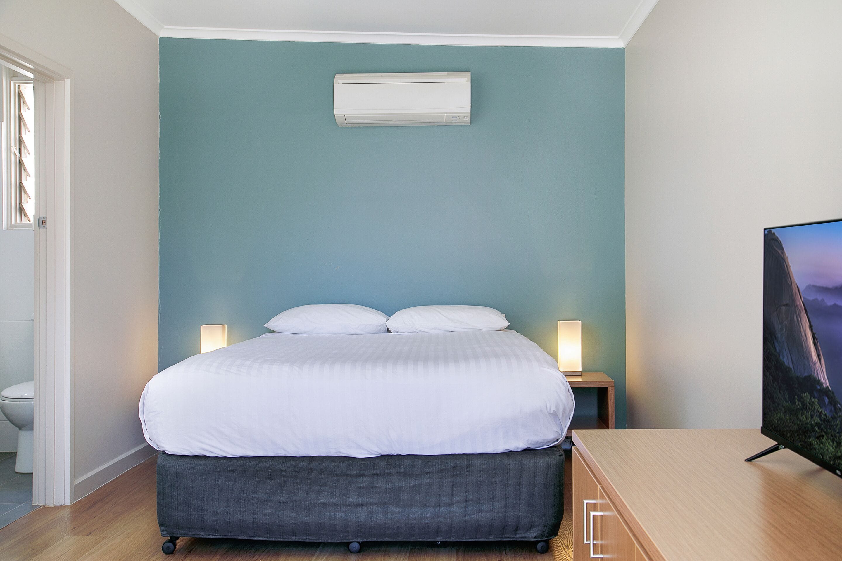A bedroom with a bed, bedside lamps, a television, and an air conditioning unit.