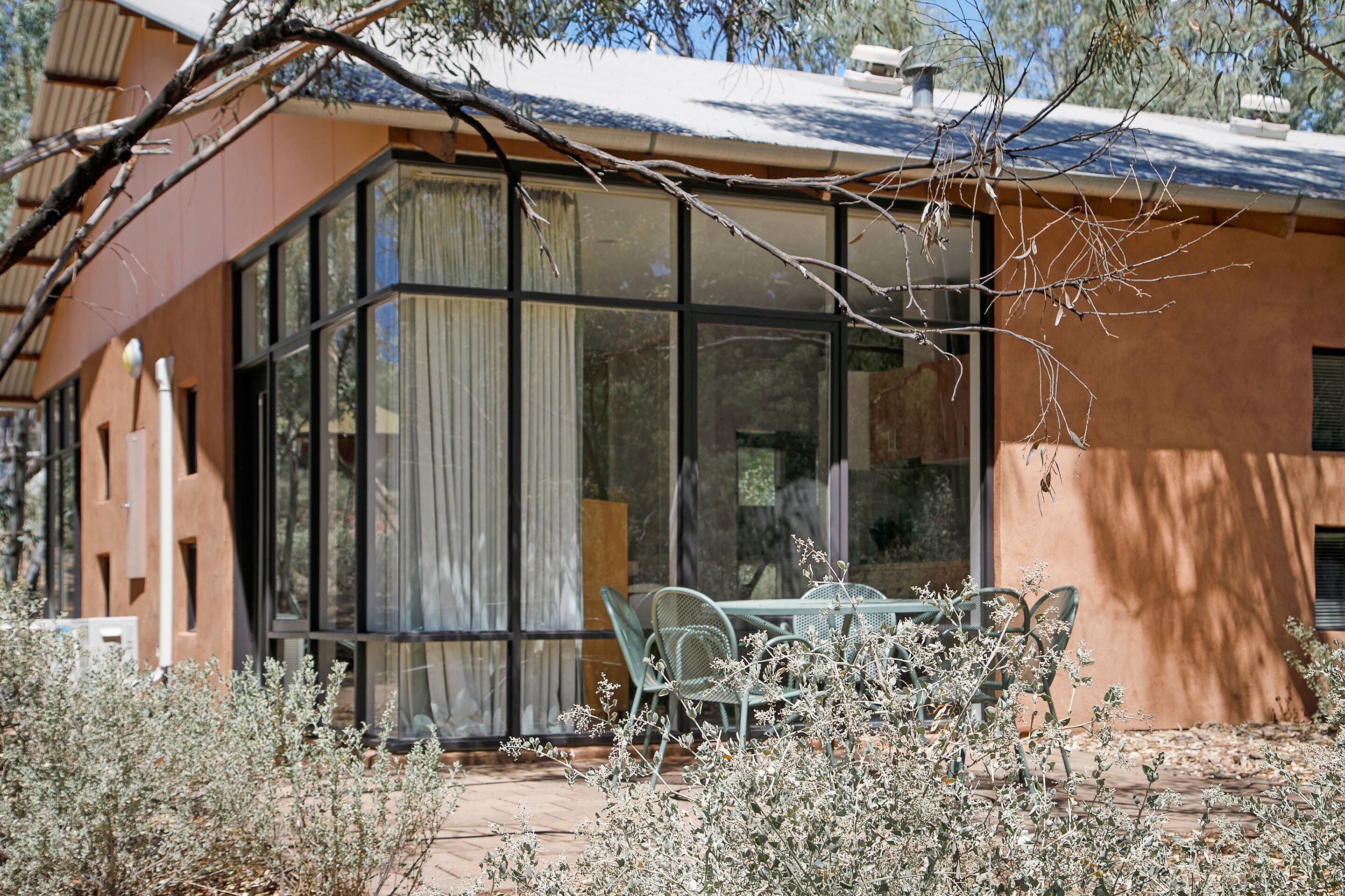 Un edificio con ventanas amplias, un patio con sillas y un árbol en primer plano.