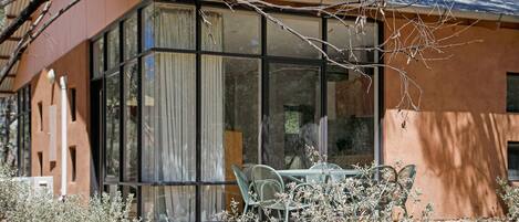 Un edificio con ventanas amplias, un patio con sillas y un árbol en primer plano.