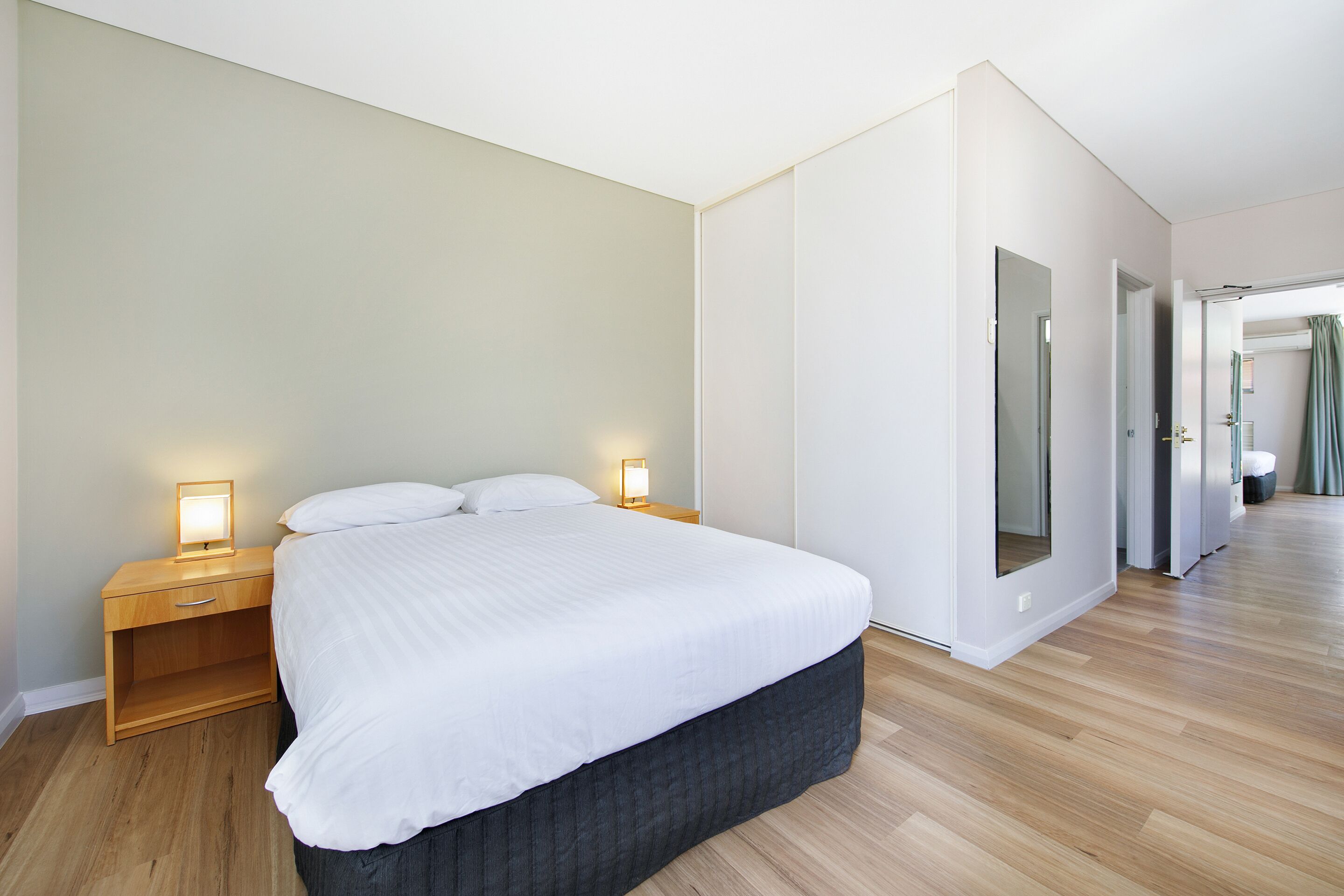 A modern bedroom with a large bed, wooden nightstands, and a mirror.