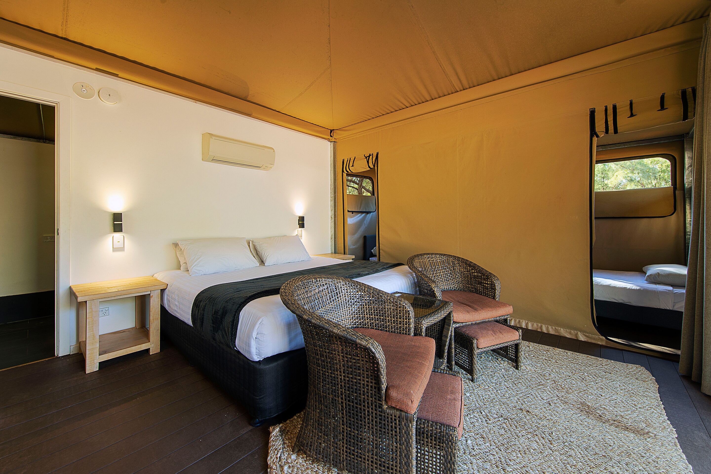 A bedroom with a bed, two wicker chairs, a small wooden nightstand, and a window with curtains.
