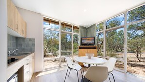 Una cocina moderna con horno integrado, un comedor con mesa y sillas redondas, y ventanas amplias con vistas al exterior.