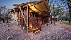 Una cabaña de madera con techo inclinado y un porche cubierto, rodeada de árboles.