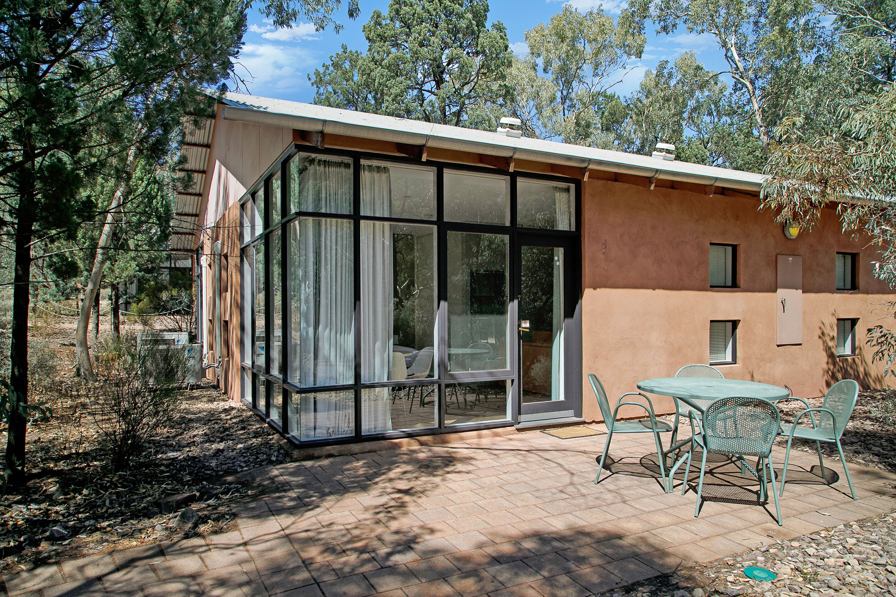 A modern house with large glass windows, a patio with outdoor furniture, and a natural surrounding.