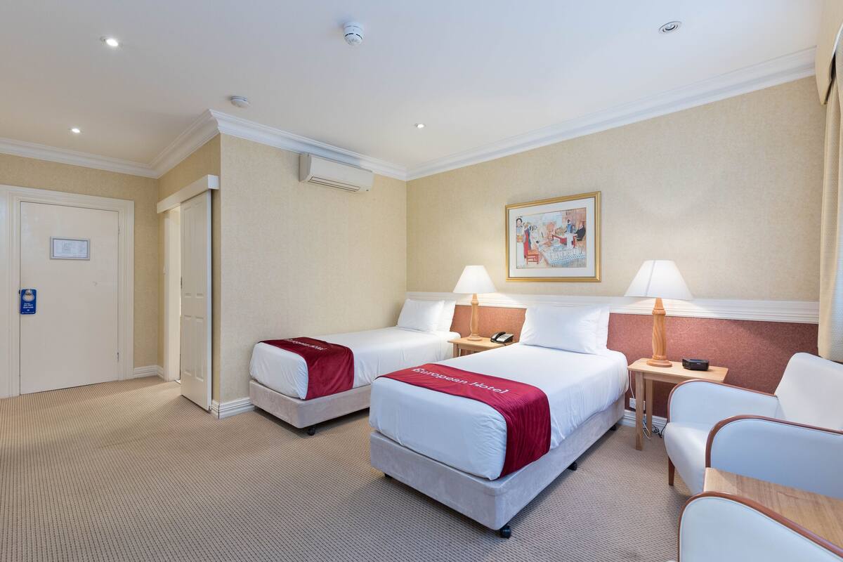 A hotel room with two beds, a desk, a chair, and a painting on the wall.