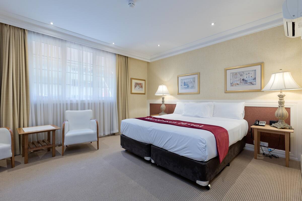 A hotel room with a large bed, two bedside tables, a chair, and a window with curtains.