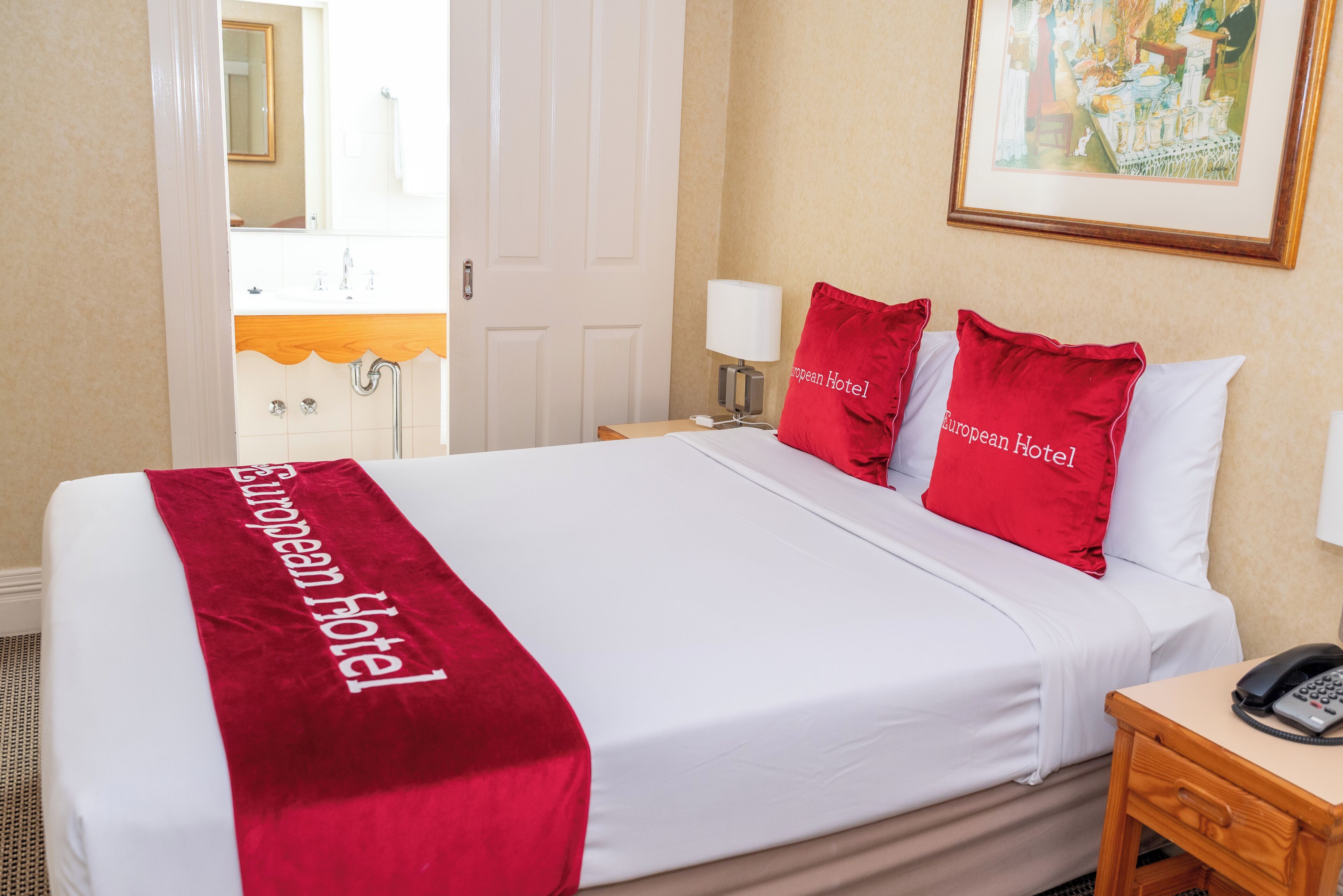 A hotel room with a bed, a nightstand, a lamp, and a painting on the wall.