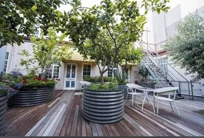 A rooftop patio with wooden flooring, metal planters with plants, a white table and chairs, and a staircase. - European Hotel (Perth)