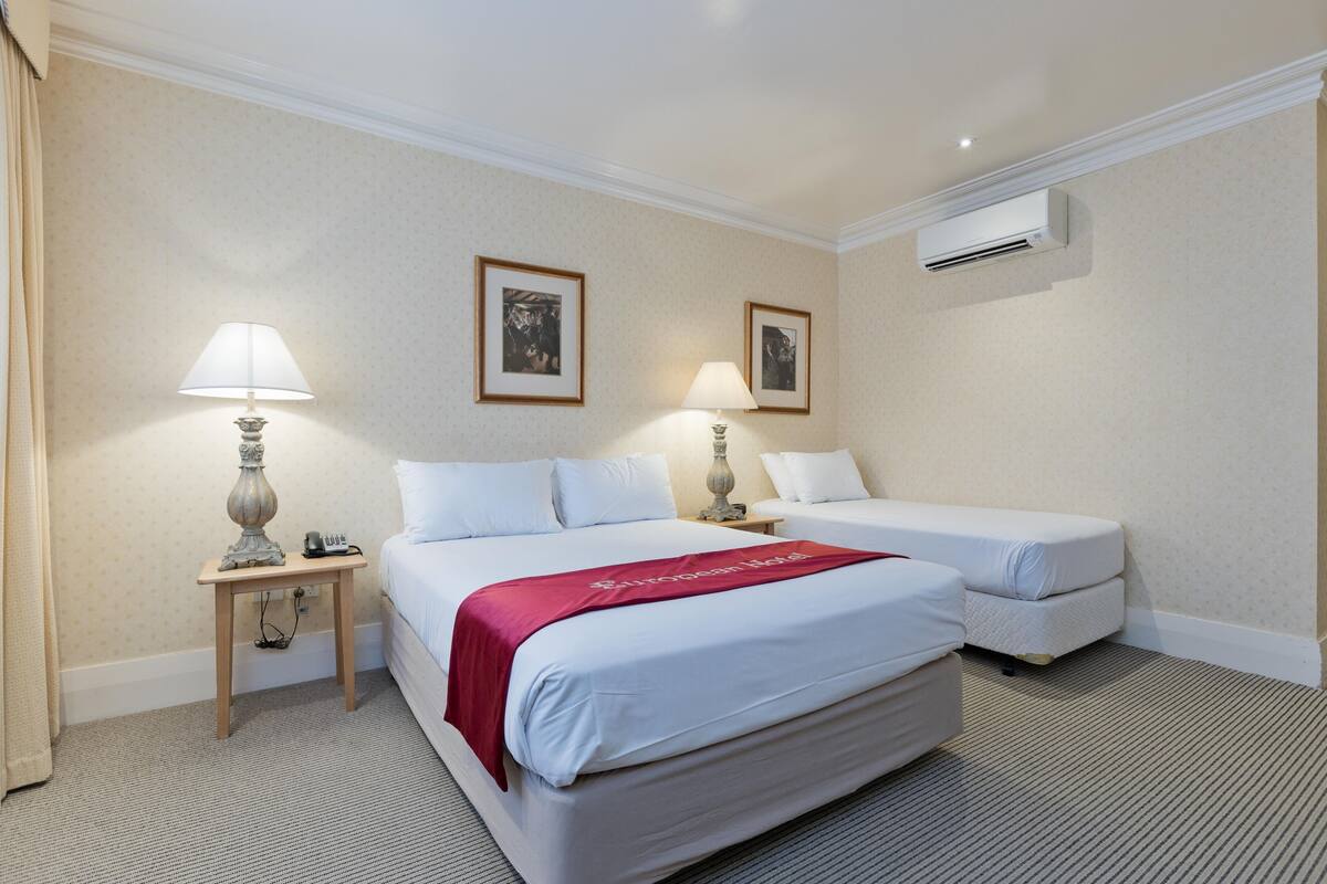 A hotel room with two beds, a nightstand with a lamp, a telephone, and two framed pictures on the wall.