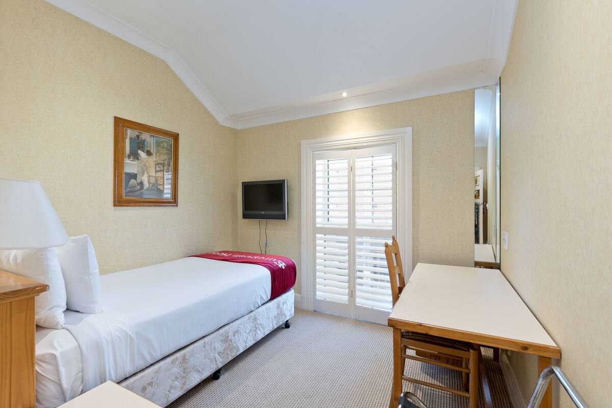 A hotel room with a bed, a desk, a chair, a television, and a door with blinds.