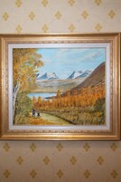 A framed landscape painting with a gold frame, set against a patterned wallpaper background.