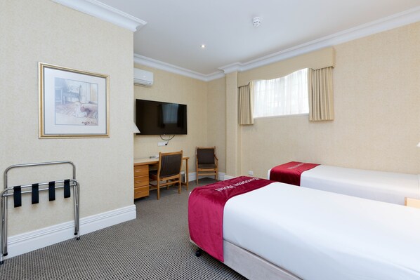 Habitación de hotel con dos camas, un escritorio, una silla, un televisor y un cuadro en la pared.
