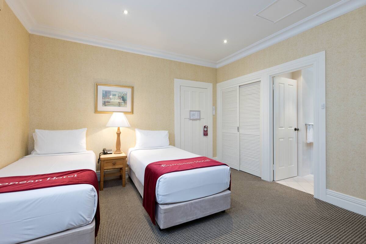 A hotel room with two beds, a nightstand, a lamp, and a framed picture on the wall.