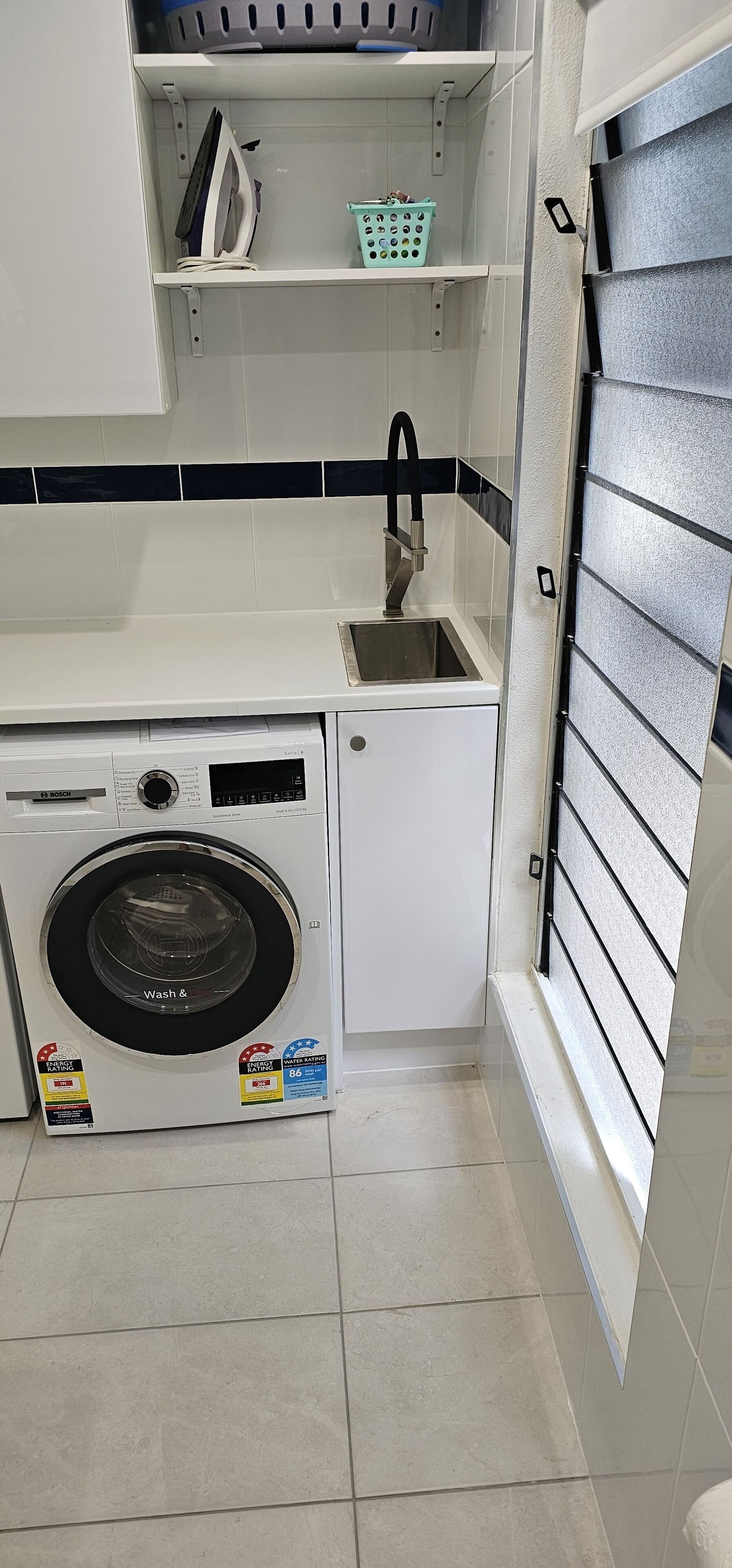 A compact laundry area with a front-loading washing machine, a sink, and a small shelf with a basket.
