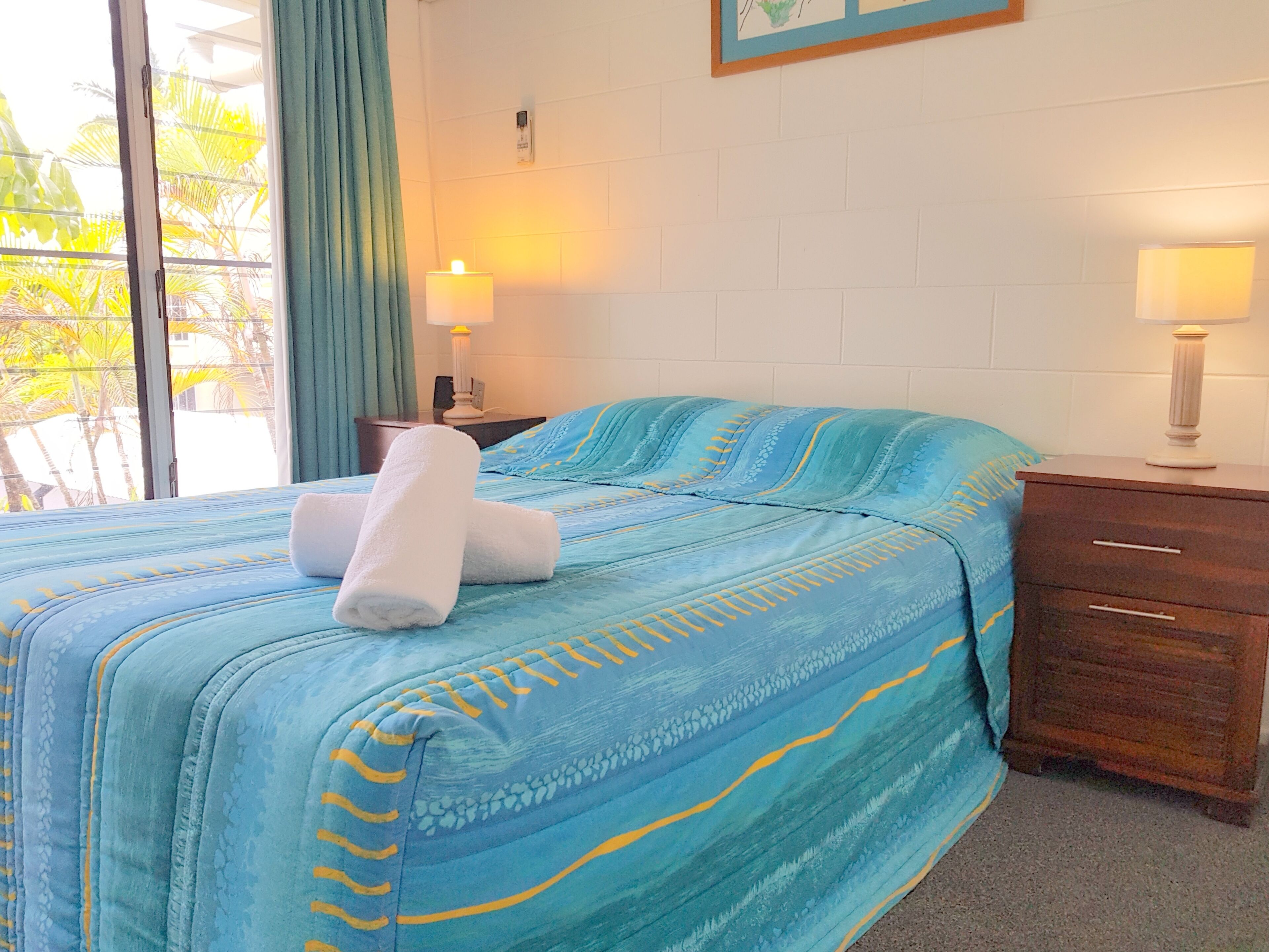 A hotel room with a bed, two bedside tables, a window with curtains, and a wall-mounted lamp.
