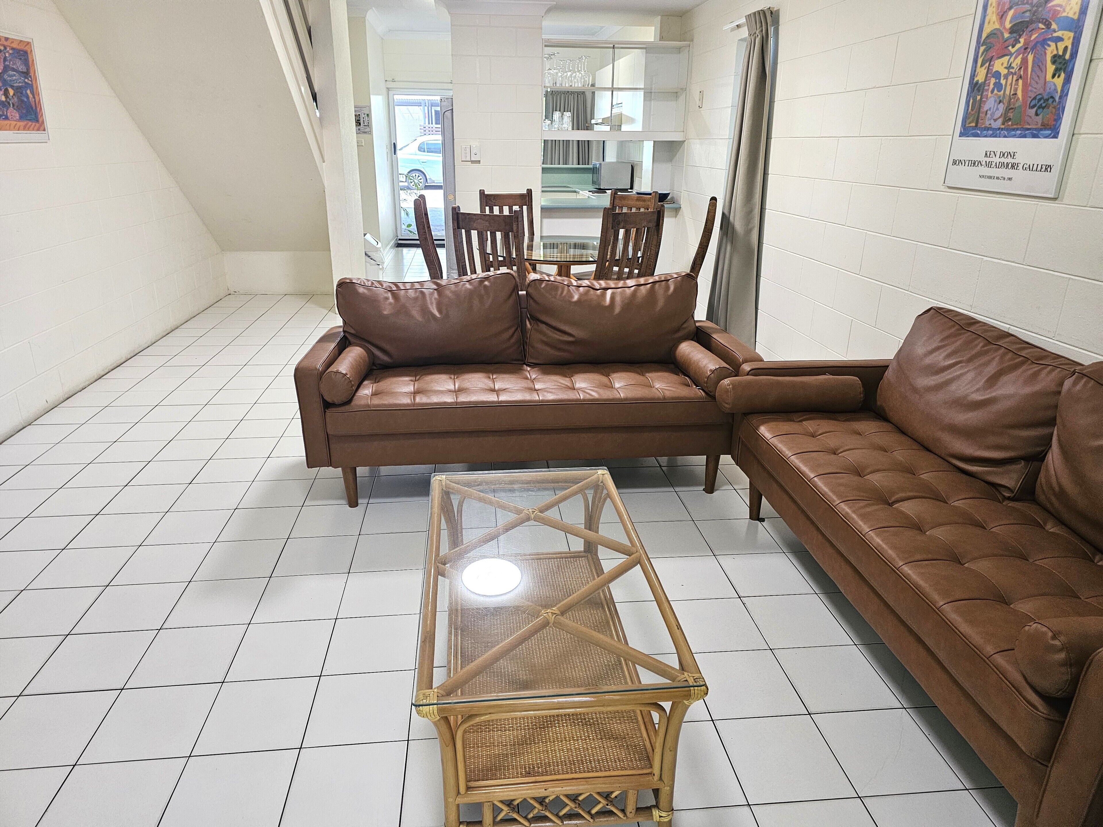 A living room with a brown leather sofa, a glass-top coffee table, and a wicker chair.
