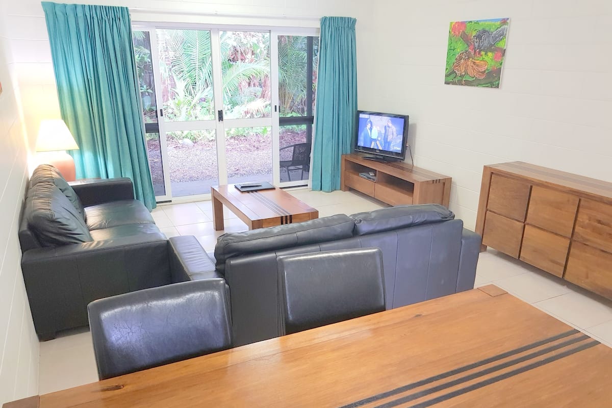 Una sala de estar con un sofá, una mesa de centro de madera, un televisor sobre un mueble de madera y un armario.