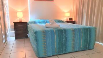 A neatly made bed with a blue and yellow striped bedspread, two bedside lamps, and a small nightstand with a lamp.