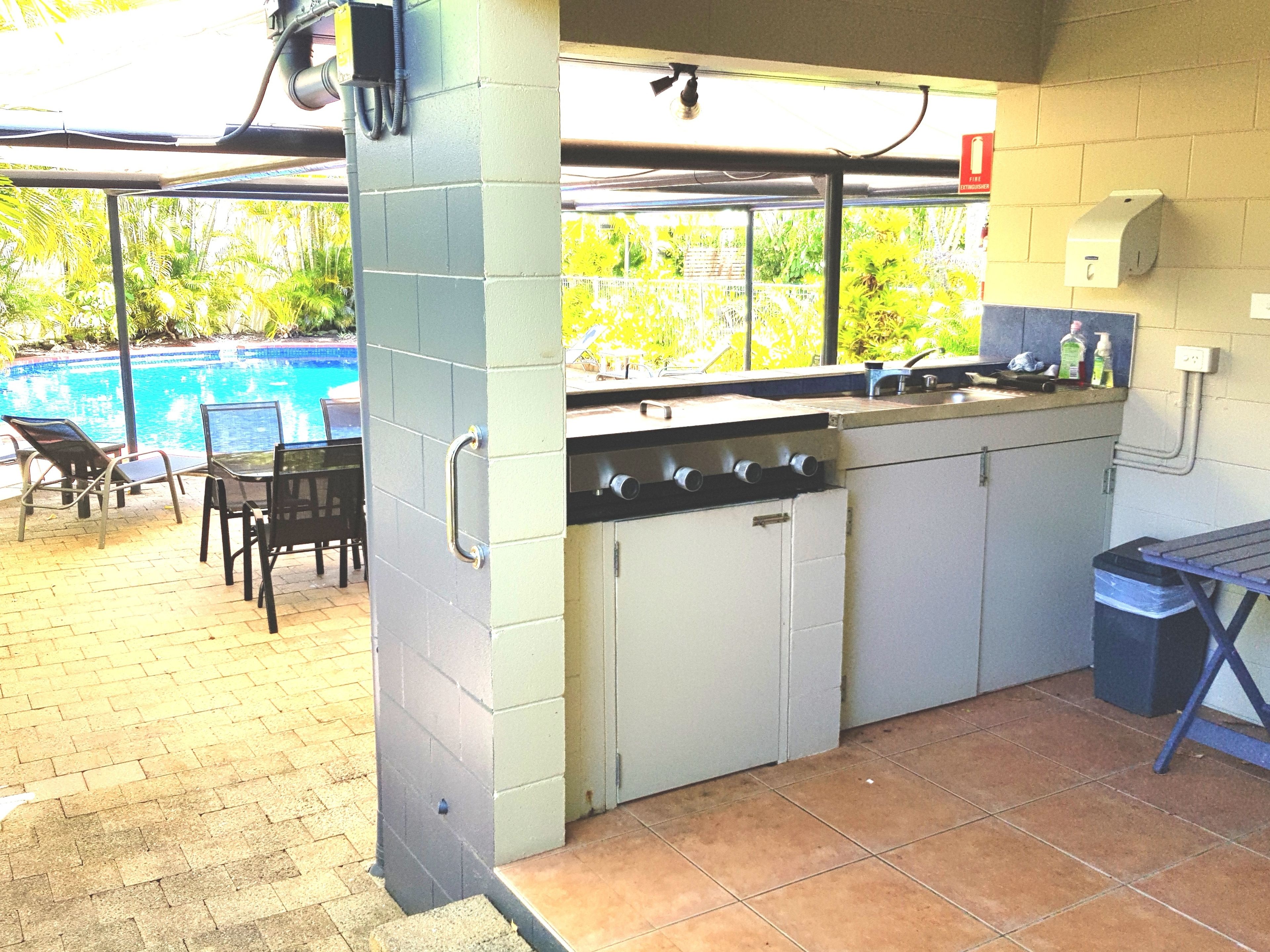 An outdoor kitchen with a grill, bar area, and seating by a pool.