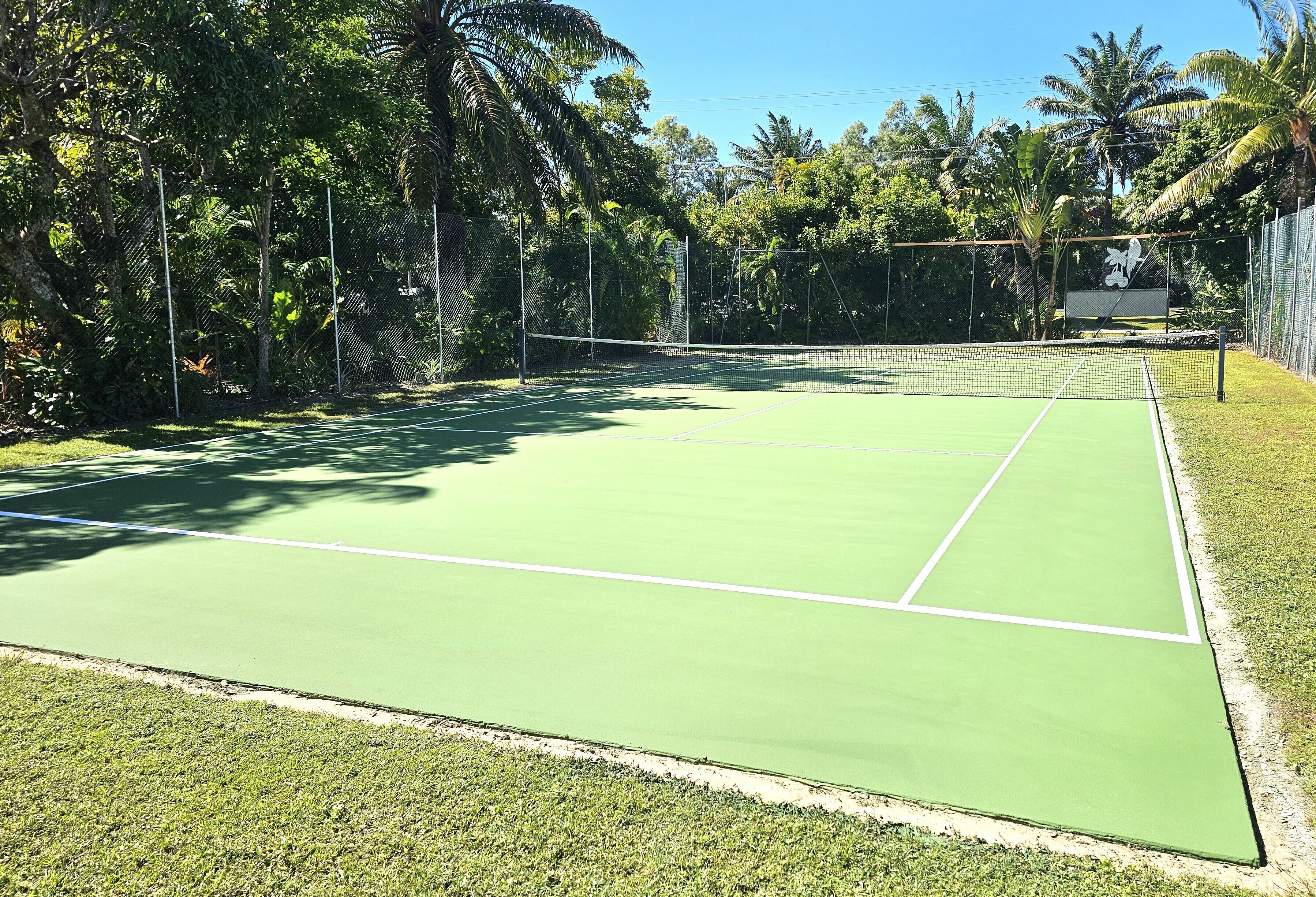 En tennisbana omgiven av frodig grönska och en klar himmel.