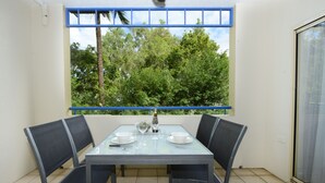 A balcony with a table set for two, chairs, and a view of trees. - Central Plaza Port Douglas Apartments (Port Douglas)