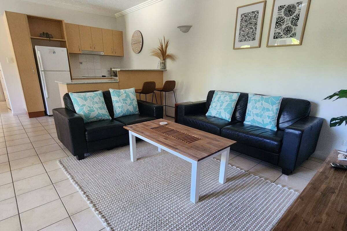 Ein modernes Wohnzimmer mit einer schwarzen Ledersofa, einem Holztisch und einer Küche im Hintergrund.
