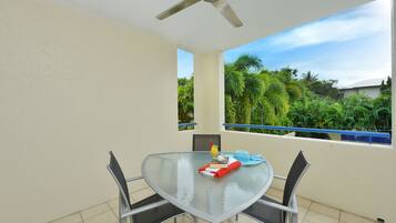 A glass table with metal chairs, a ceiling fan, and a view of greenery outside.