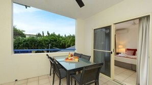 A balcony with a glass table and chairs, a view of greenery, and a sliding glass door leading to a bedroom. - Central Plaza Port Douglas Apartments (Port Douglas)