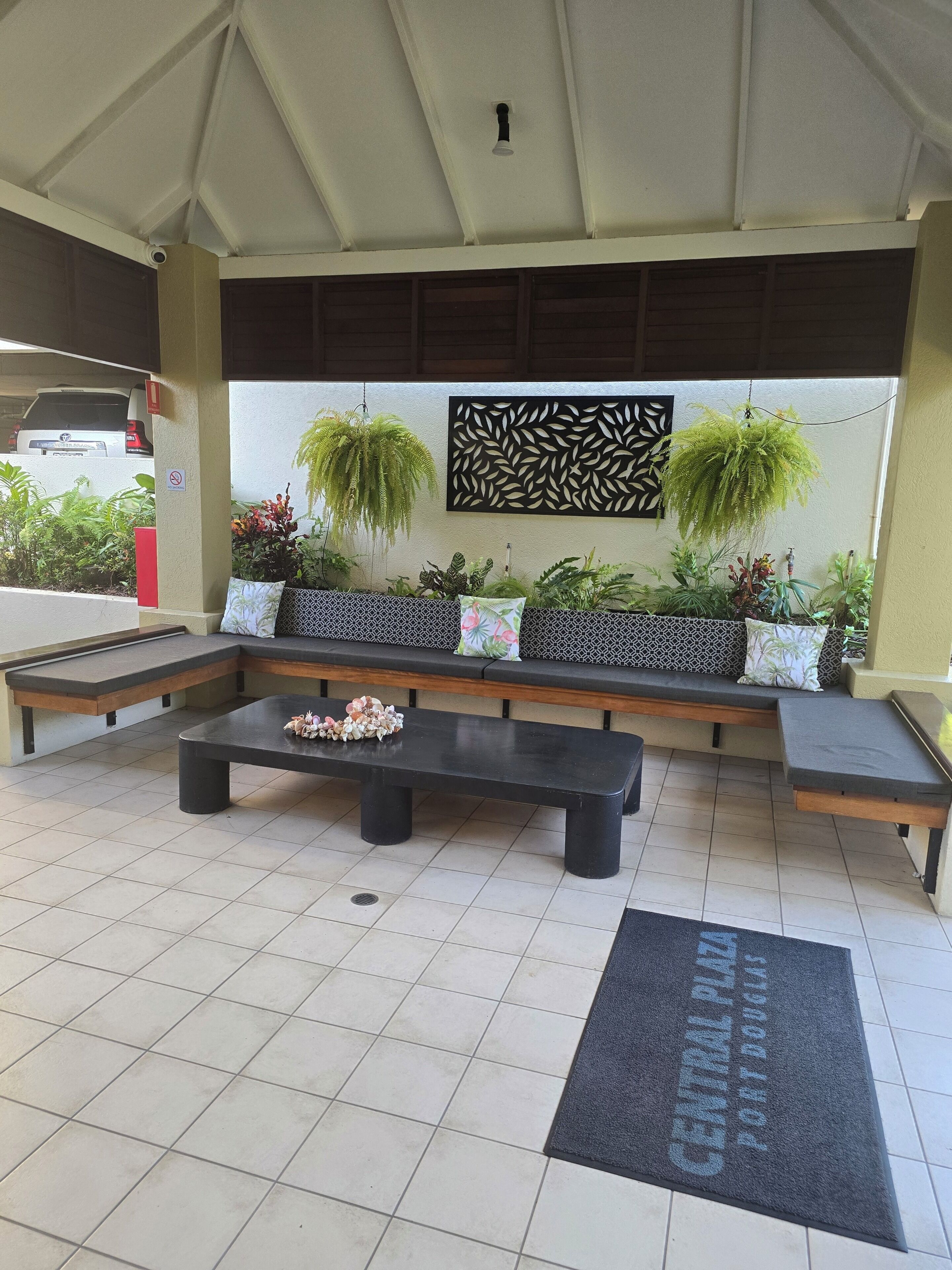 A covered outdoor seating area with a bench, a coffee table, and potted plants.