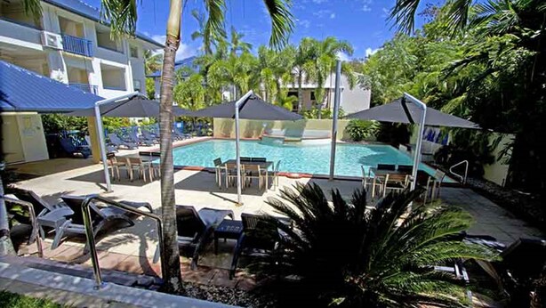 A pool area with lounge chairs and umbrellas, surrounded by palm trees and a building with balconies. - Central Plaza Port Douglas Apartments (Port Douglas)